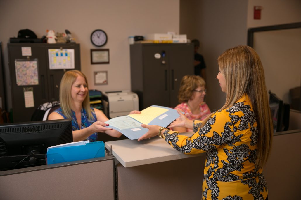 Woman handing folder over counter to another woman